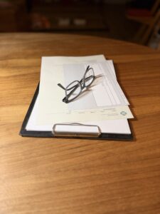 Brille liegt auf Anmeldeunterlagen auf einem Holztisch